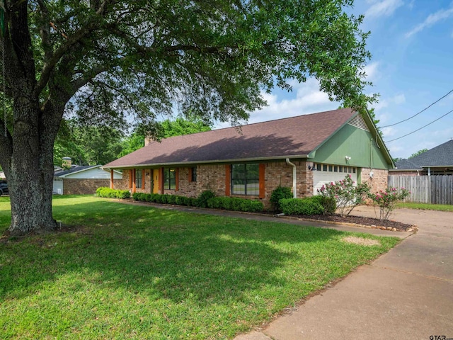 ranch-style house featuring driveway, a chimney, a front yard, brick siding, and an attached garage