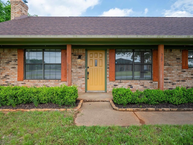 property entrance with covered porch, brick siding, a chimney, and roof with shingles