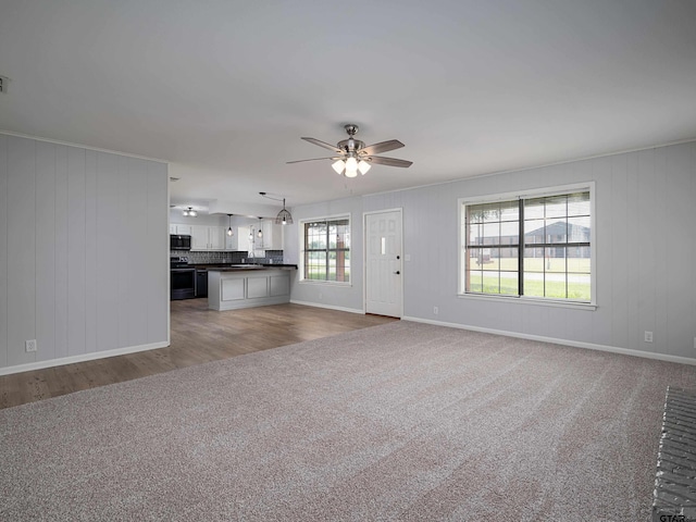 unfurnished living room with carpet flooring, a ceiling fan, baseboards, and wood finished floors