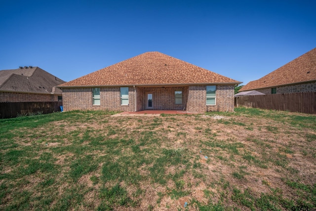 rear view of house featuring a patio, a fenced backyard, brick siding, a shingled roof, and a lawn