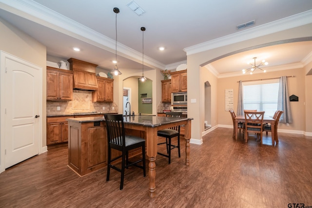 kitchen with visible vents, brown cabinetry, arched walkways, appliances with stainless steel finishes, and a kitchen breakfast bar