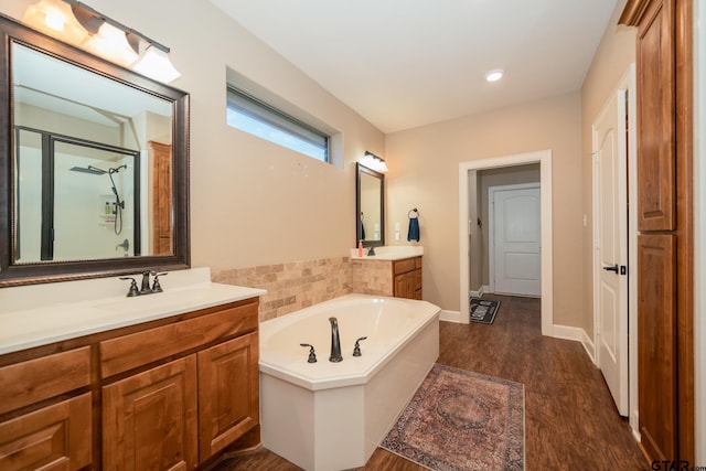 bathroom with wood finished floors, two vanities, a sink, a bath, and an enclosed shower