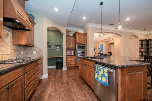 kitchen featuring appliances with stainless steel finishes, brown cabinets, dark wood-style flooring, a kitchen island with sink, and a sink