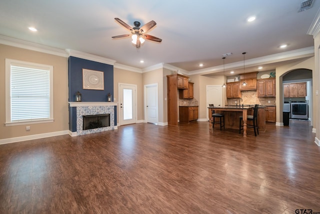 unfurnished living room featuring a tiled fireplace, visible vents, dark wood-style flooring, and ornamental molding