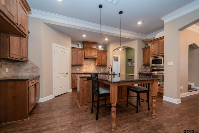 kitchen with arched walkways, appliances with stainless steel finishes, a breakfast bar area, and brown cabinets