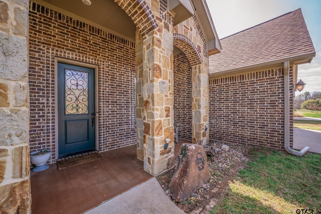 property entrance with stone siding, a shingled roof, and brick siding