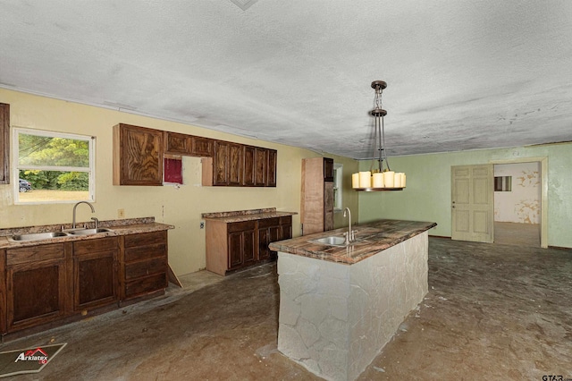 kitchen with pendant lighting, a textured ceiling, sink, and an island with sink