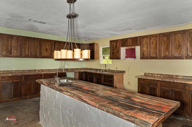 kitchen featuring a textured ceiling, dark brown cabinetry, hanging light fixtures, and sink