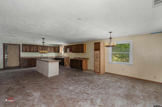 kitchen featuring a textured ceiling, decorative light fixtures, a kitchen island, and sink