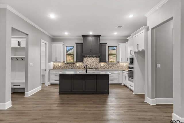 kitchen featuring white cabinetry, stainless steel appliances, dark hardwood / wood-style floors, an island with sink, and ornamental molding