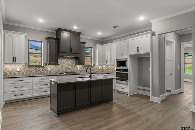 kitchen featuring light wood-type flooring, ornamental molding, stainless steel appliances, sink, and a center island with sink