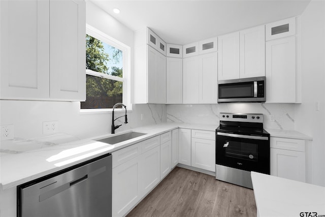 kitchen with light hardwood / wood-style floors, stainless steel appliances, light stone counters, white cabinets, and sink