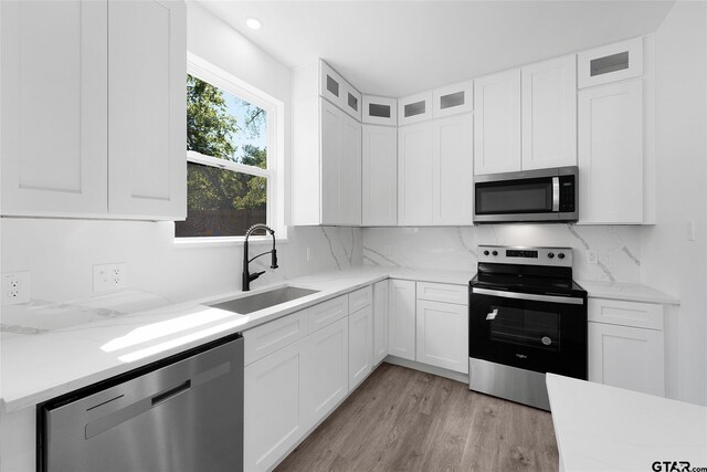 kitchen with light hardwood / wood-style floors, stainless steel appliances, light stone counters, white cabinets, and sink