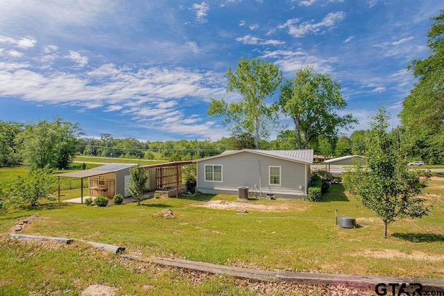 rear view of house featuring a detached carport, a lawn, an outdoor structure, and central AC unit