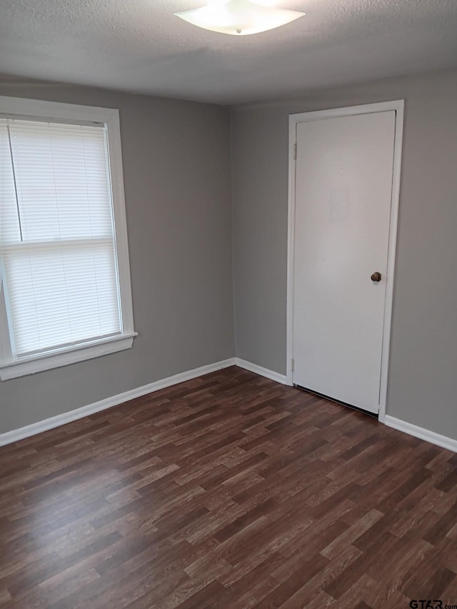 unfurnished room with baseboards, a textured ceiling, and dark wood-style floors