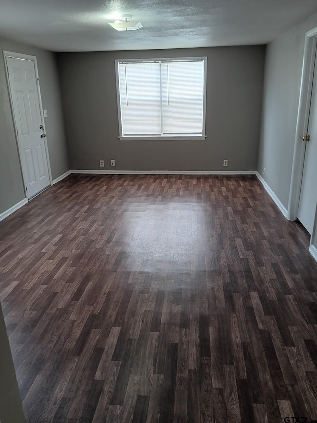 empty room with dark wood finished floors, a textured ceiling, and baseboards