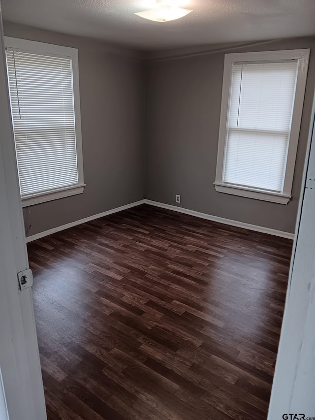 spare room featuring a textured ceiling, dark wood-type flooring, and baseboards