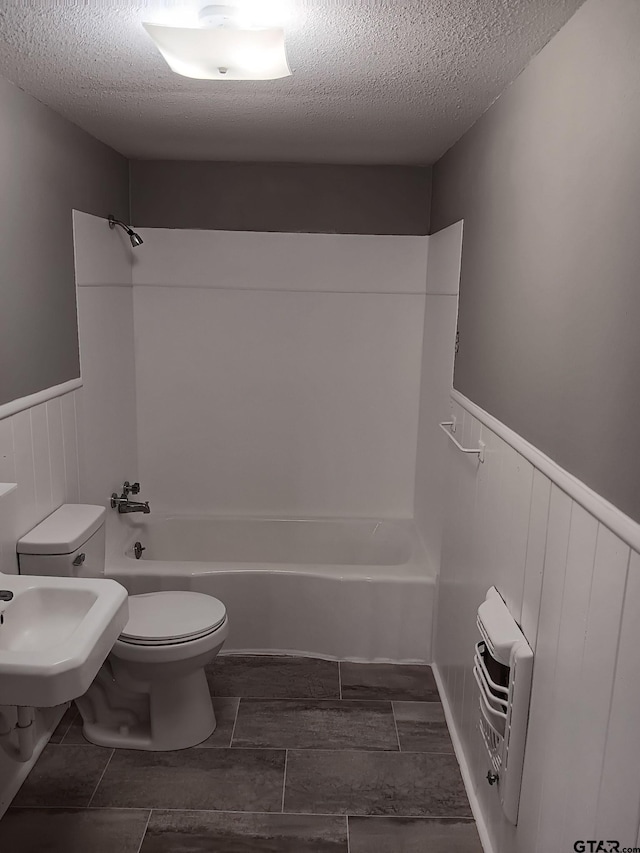 bathroom with wainscoting, a textured ceiling, toilet, and tub / shower combination