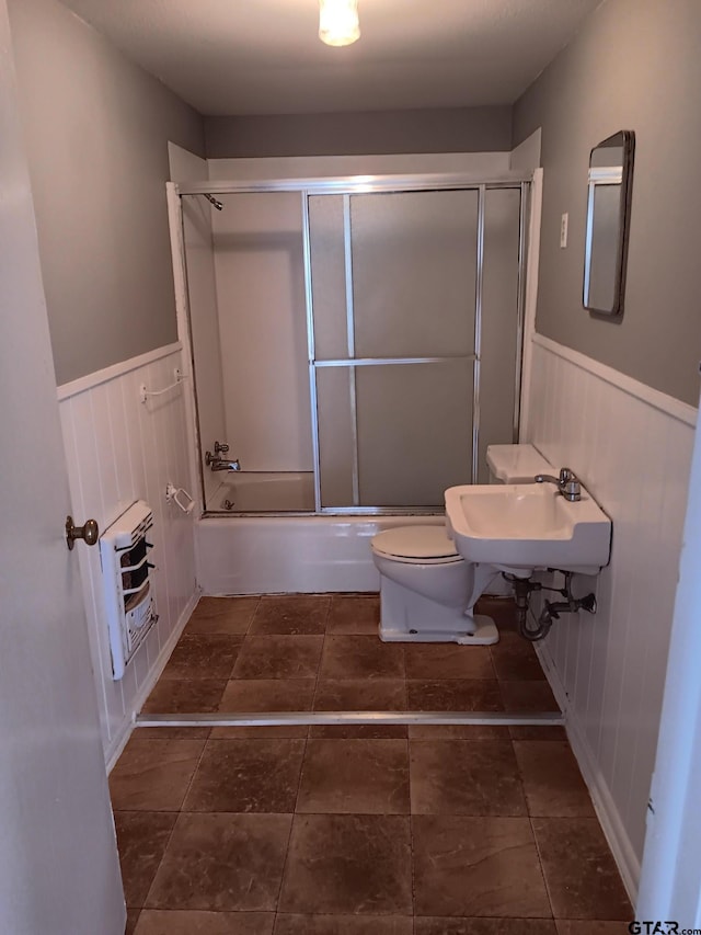 bathroom featuring enclosed tub / shower combo, wainscoting, toilet, and a sink