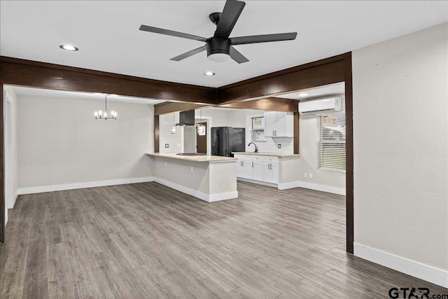 unfurnished living room with sink, ceiling fan with notable chandelier, a wall mounted air conditioner, and hardwood / wood-style flooring