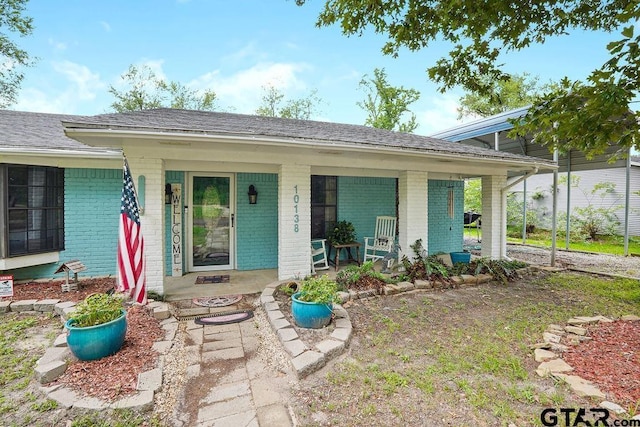 exterior space with roof with shingles, a porch, and brick siding