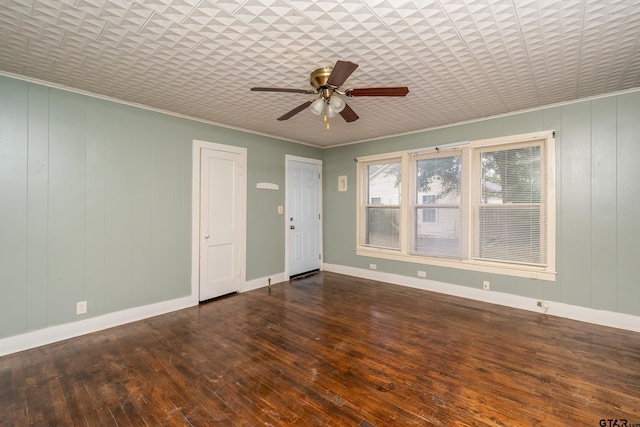 empty room with dark hardwood / wood-style flooring, wood walls, ceiling fan, and ornamental molding