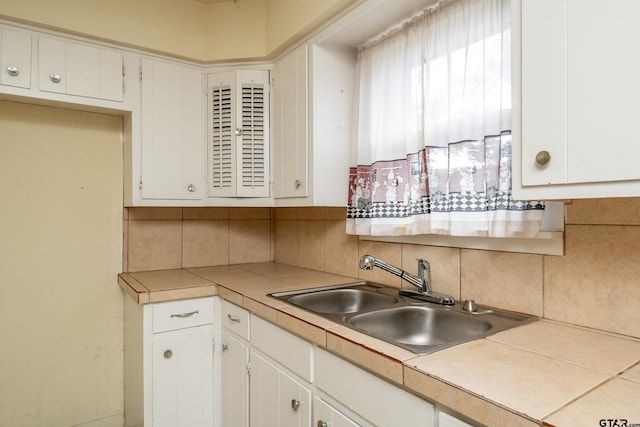 kitchen featuring white cabinets, tile countertops, sink, and tasteful backsplash