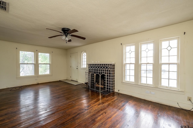 unfurnished living room featuring dark hardwood / wood-style flooring, a tiled fireplace, a textured ceiling, and ceiling fan