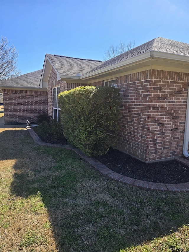 view of side of property featuring brick siding, a lawn, and a shingled roof