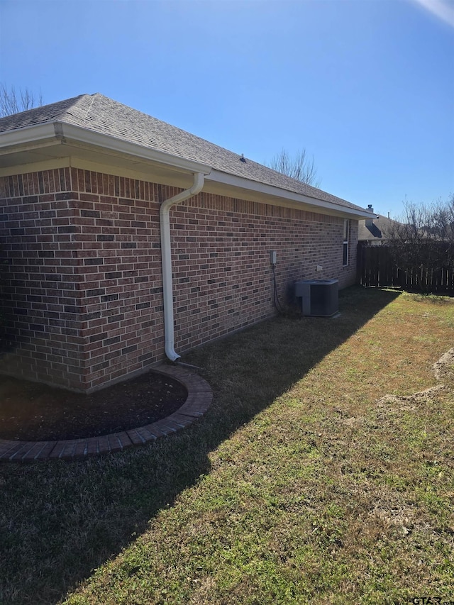 view of side of property featuring fence, a lawn, cooling unit, and brick siding