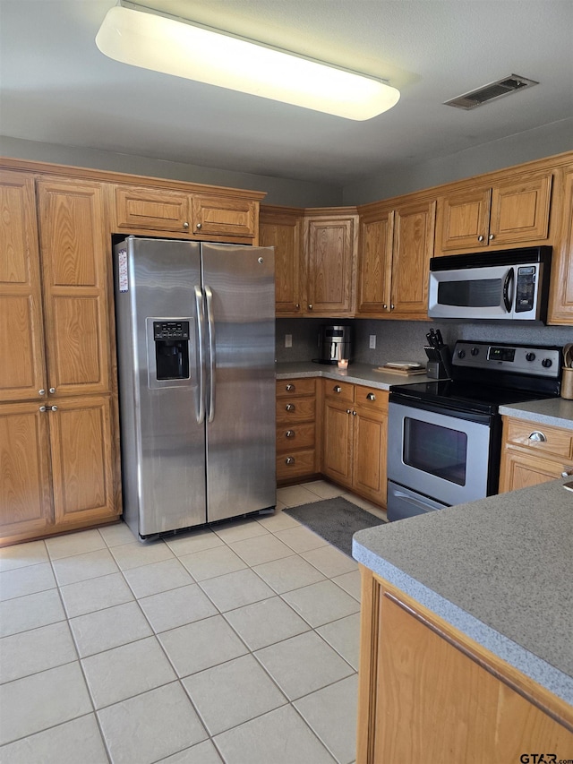 kitchen with stainless steel appliances, brown cabinetry, visible vents, and light tile patterned flooring