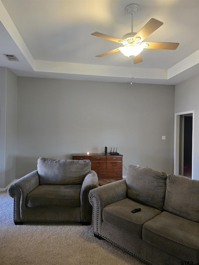 carpeted living area with visible vents, a tray ceiling, and ceiling fan