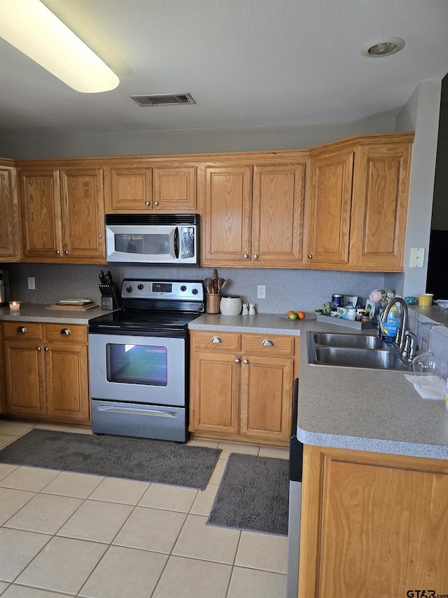 kitchen with light tile patterned floors, visible vents, brown cabinetry, stainless steel appliances, and a sink