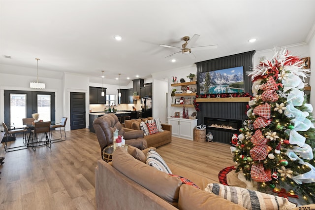 living room with ceiling fan, light hardwood / wood-style floors, ornamental molding, and a fireplace