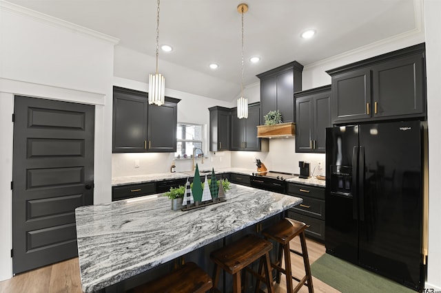 kitchen featuring black fridge, ornamental molding, a kitchen island, hanging light fixtures, and a breakfast bar area