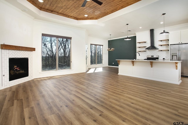 unfurnished living room featuring a tile fireplace, ceiling fan with notable chandelier, wood ceiling, and a tray ceiling