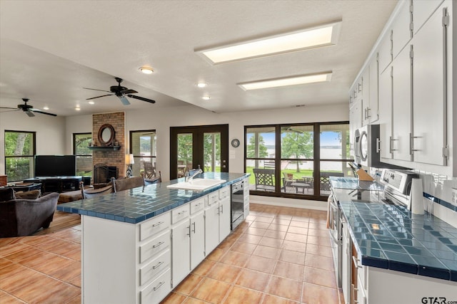 7016 Fm 3054, Malakoff, TX 75148 - kitchen with tile countertops, stainless steel appliances, a sink, a brick fireplace, and white cabinetry