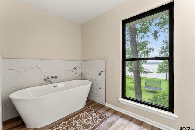 7016 Fm 3054, Malakoff, TX 75148 - bathroom featuring tile walls, a soaking tub, wood finished floors, and wainscoting