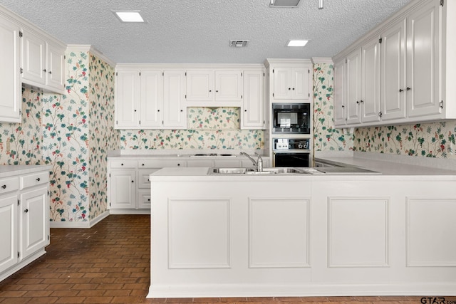 kitchen with black appliances, crown molding, white cabinetry, and sink