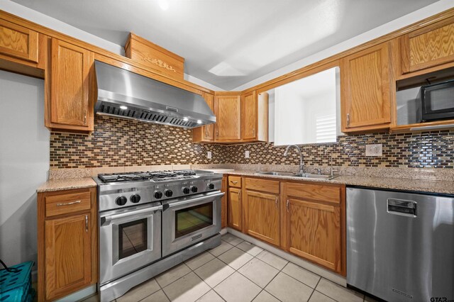 kitchen with light stone countertops, sink, stainless steel appliances, wall chimney range hood, and backsplash