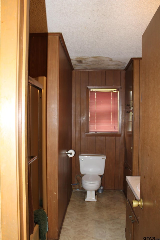 bathroom featuring vanity, wooden walls, toilet, and a textured ceiling