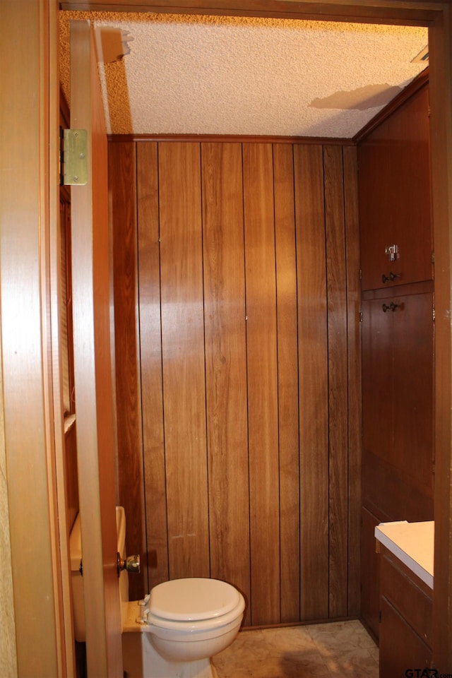 bathroom with vanity, a textured ceiling, toilet, and wood walls