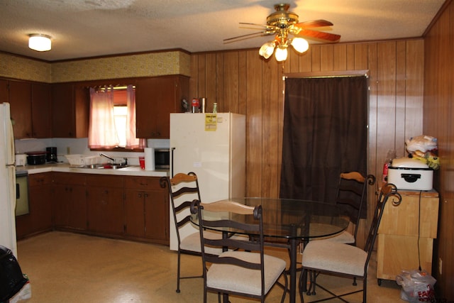 kitchen with sink, wood walls, a textured ceiling, white fridge, and ceiling fan