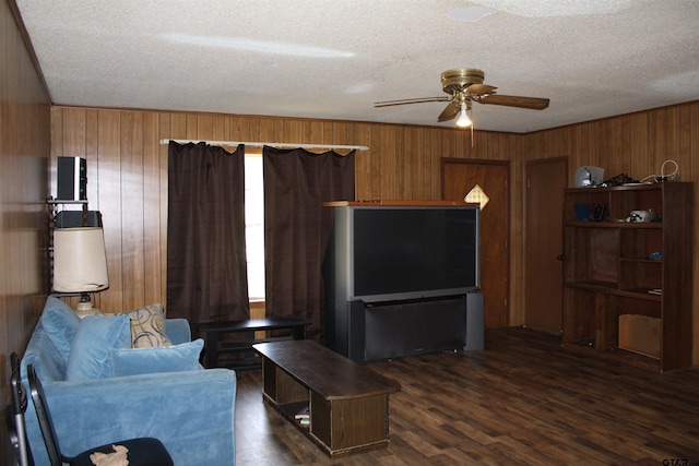 living room with dark hardwood / wood-style flooring, ceiling fan, wooden walls, and a textured ceiling