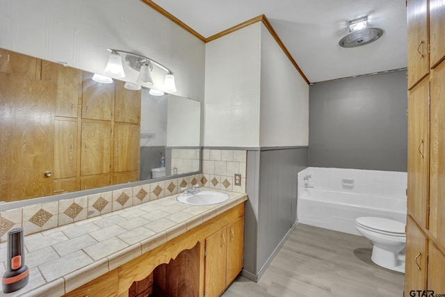 bathroom with a garden tub, toilet, wood finished floors, crown molding, and vanity