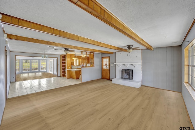 unfurnished living room with a ceiling fan, wood finished floors, a fireplace, a textured ceiling, and beamed ceiling