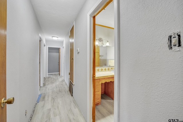 hallway featuring light wood-style floors, baseboards, and a textured wall