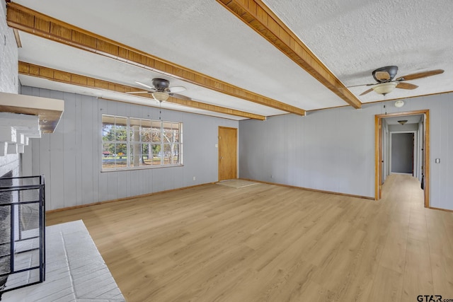 unfurnished living room featuring ceiling fan, beam ceiling, light wood-type flooring, and a textured ceiling