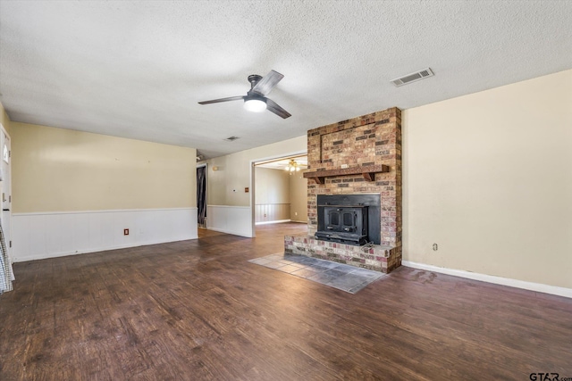 unfurnished living room featuring a wood stove, dark hardwood / wood-style flooring, a textured ceiling, and ceiling fan