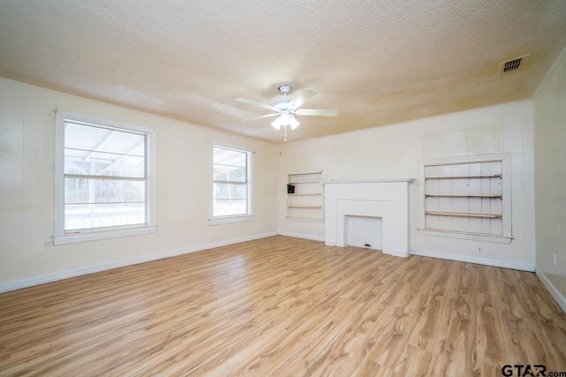 unfurnished living room with built in shelves, a textured ceiling, light hardwood / wood-style floors, and ceiling fan